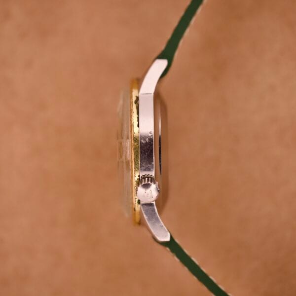 Side view of a Wyler Dynawind Heavy Duty 660 Life Guard wristwatch with a silver crown and green strap, set against a brown background.