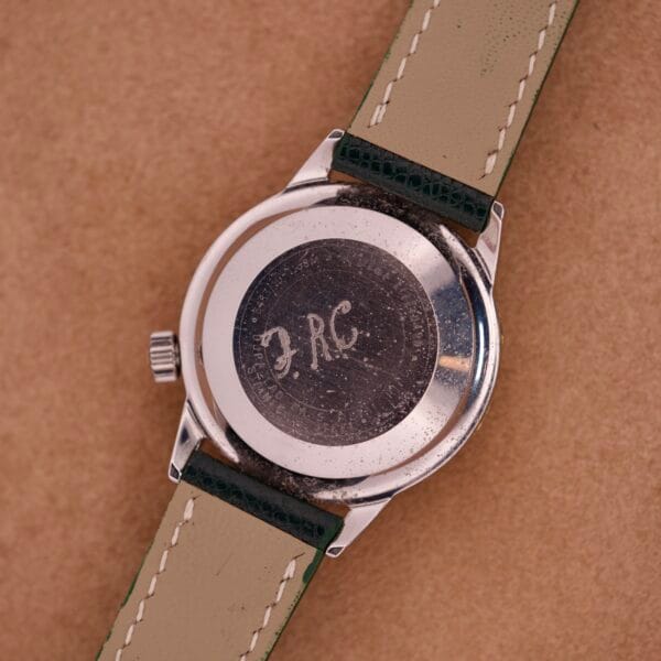 A close-up of a Wyler Dynawind Heavy Duty 660 Life Guard watch back engraved with “JRC” and “Heavy Duty 660,” resting on a brown surface.