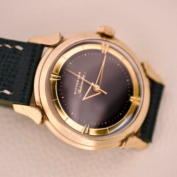 Wittnauer Automatic Black Gilt Dial Cal. 11ARG wristwatch with a black leather strap, elegantly showcased on a light surface.