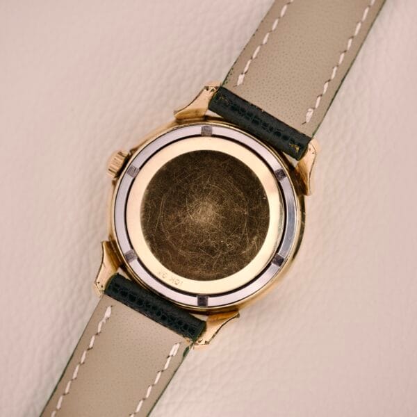 The back of a Wittnauer Automatic Black Gilt Dial Cal. 11ARG wristwatch with a scratched case and beige leather strap rests on a light surface.