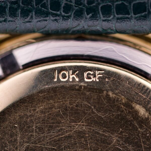 Close-up of a Wittnauer Automatic Black Gilt Dial Cal. 11ARG, showing its gold 10K GF case back beneath a green textured strap.