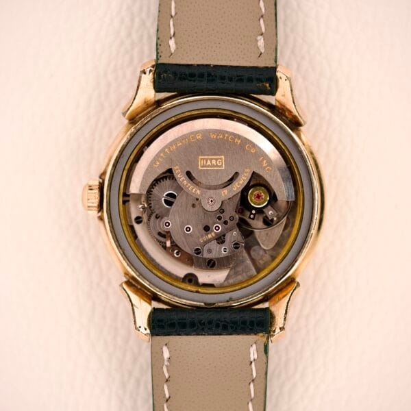 Close-up of the Wittnauer Automatic Black Gilt Dial featuring an exposed Cal. 11ARG movement and gears, complemented by a green and beige leather strap.