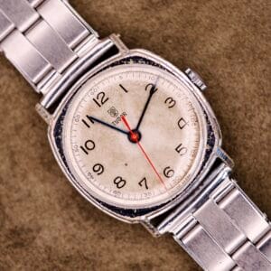A Tudor Cushion Case Trench Watch Circa 1930s with a silver band and aged white dial rests on a brown textured surface.