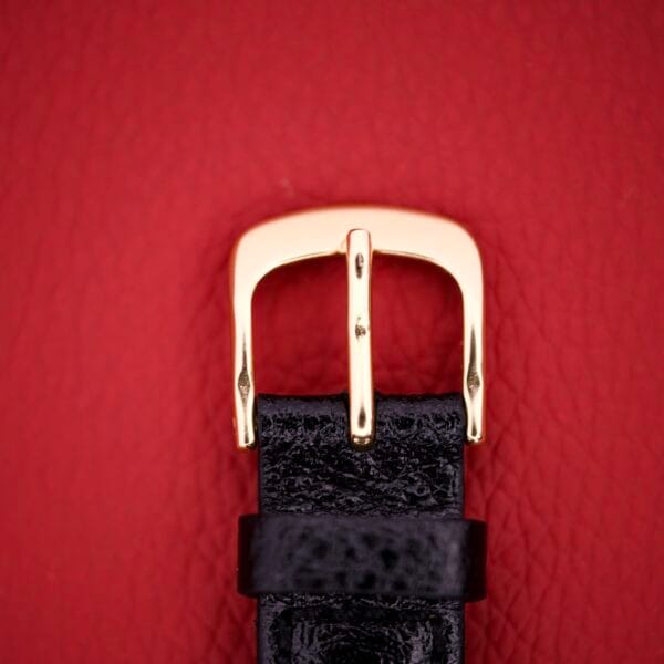 The Mido Multifort Grand Luxe Super Automatic 14k Gold Capped watch features a luxurious gold design shown against a textured red background.