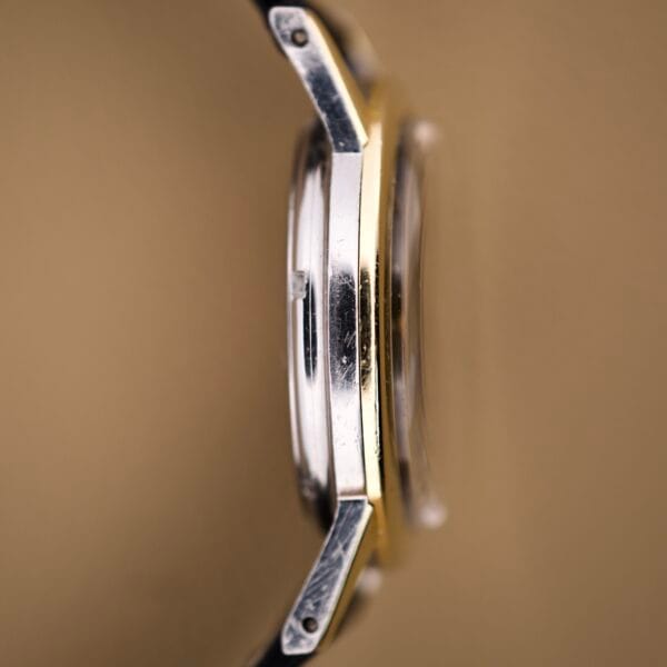 Side view of an Eterna Matic Black Dial 14k Gold Capped Case wristwatch, highlighting the bezel, crown, and lugs set against a brown background.