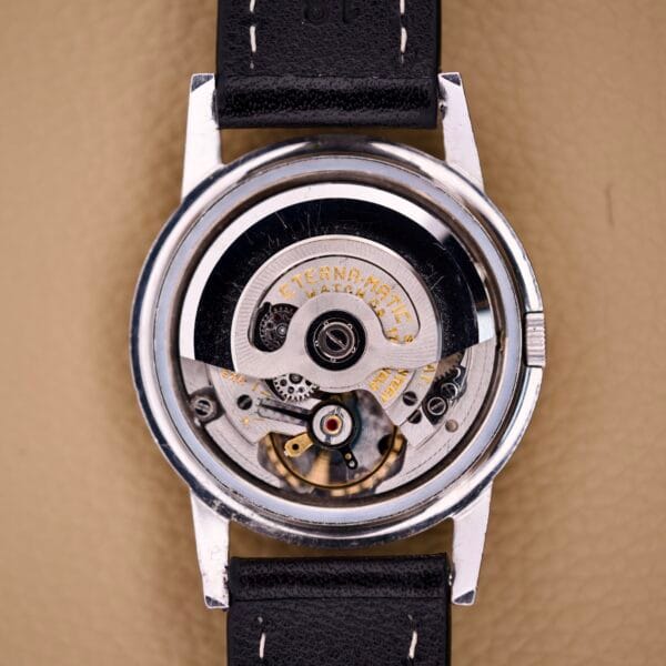 Close-up of the Eterna Matic Black Dial 14k Gold Capped Case watch, showing the ETERNA-MATIC engraved movement, a black leather strap, and a black dial with elegant 14k gold accents.