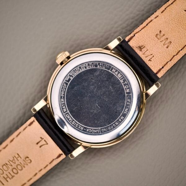 Back of a Hamilton Caliber 671 Manual Wind Black Gilt Dial watch with leather straps, displaying engravings and brand details on the case, referencing the manual wind Hamilton Caliber 671 movement inside.