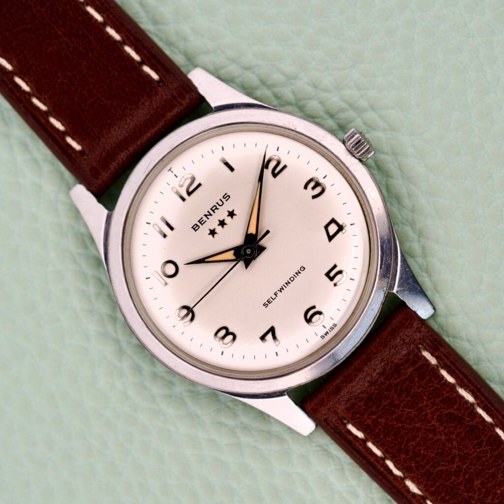 A Benrus 3 Star Automatic #7001 Series Stainless Steel wristwatch with a brown leather strap rests on a light textured surface.