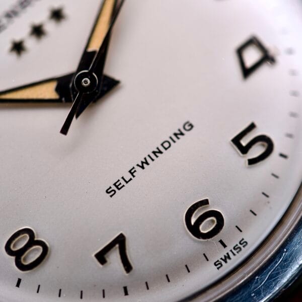 Close-up of the Benrus 3 Star Automatic #7001 Series Stainless Steel watch face, displaying the numbers 4-8 and the word “SELFWINDING.”.