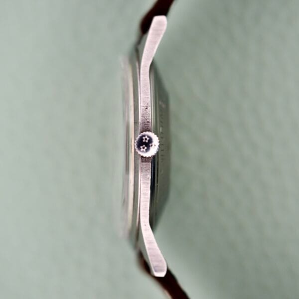 Side view of the Benrus 3 Star Automatic #7001 Series Stainless Steel watch, showcasing its star-designed crown against a lightly textured background.