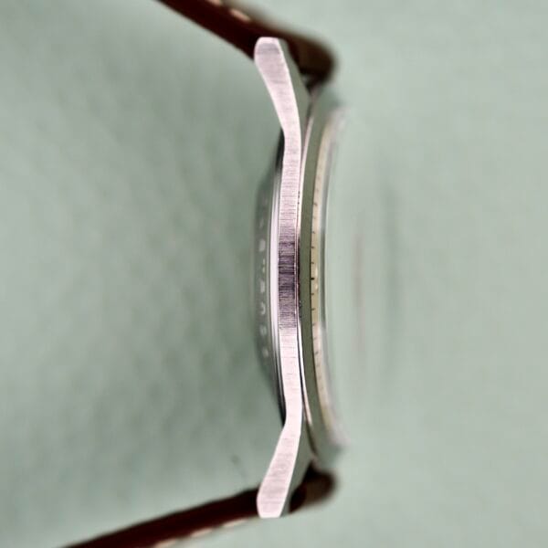 Side view of a Benrus 3 Star Automatic #7001 Series Stainless Steel wristwatch case with a brown strap, highlighting its curved, brushed stainless steel edge.