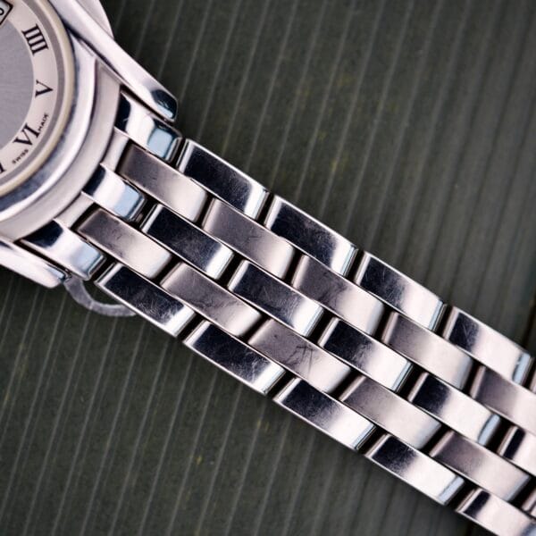 Close-up of a Gucci 5500L Stainless Steel Quartz Box & Papers watch band and part of the watch face on a textured green background.