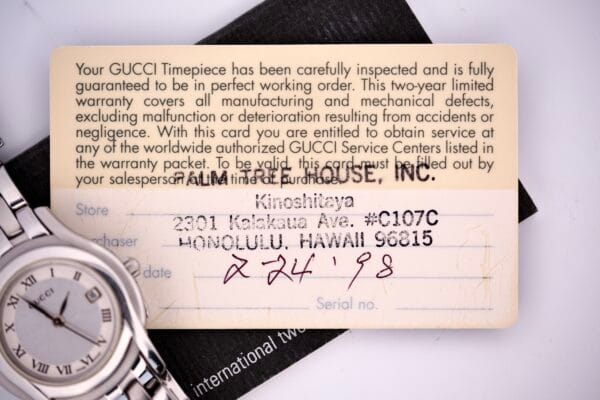 A close-up of a Gucci 5500L Stainless Steel Quartz Box & Papers warranty card, featuring part of the silver watch and a handwritten date: 2-24-98.