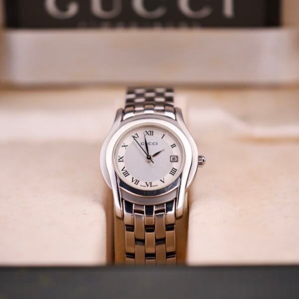 Gucci 5500L stainless steel quartz wristwatch with Roman numerals, brand logo on the dial, and includes display box and papers.