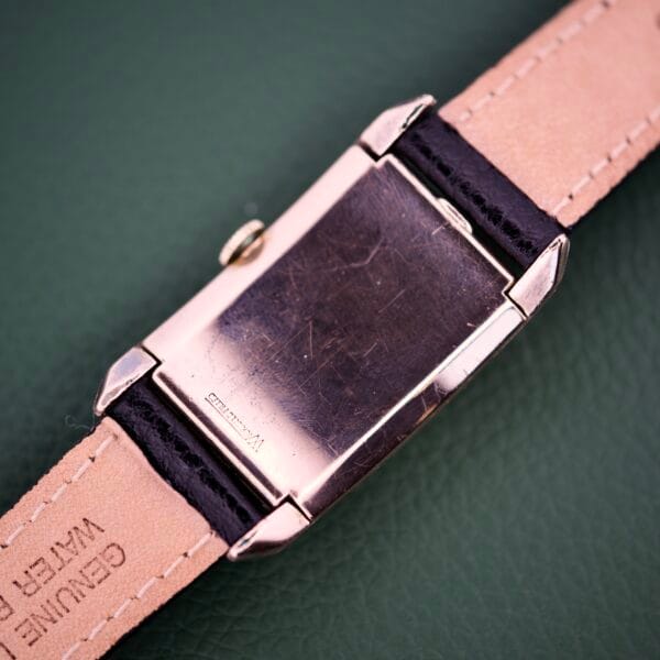 A Gruen Curvex Precision Ref. 440-448 Rose Gold Filled wristwatch with a tan leather strap rests on a green textured surface, displaying its rose gold filled case back.