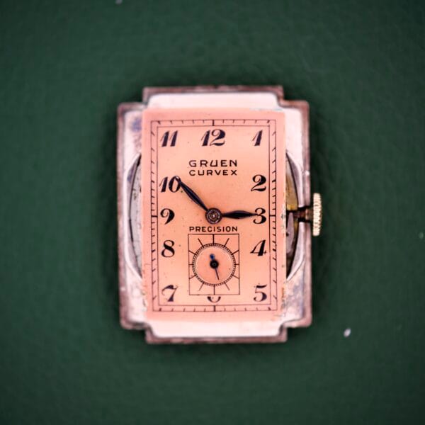 The Gruen Curvex Precision Ref. 440-448 features a rectangular rose gold filled case, vintage pink dial with black numbers on green accents—combining timeless elegance and iconic design.