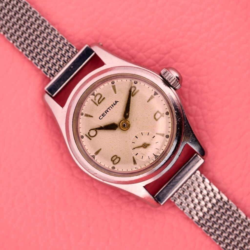 Ladies Certina Ref. 41101 wristwatch in stainless steel Cal. 19-10 with a mesh band, displayed on a pink textured background.