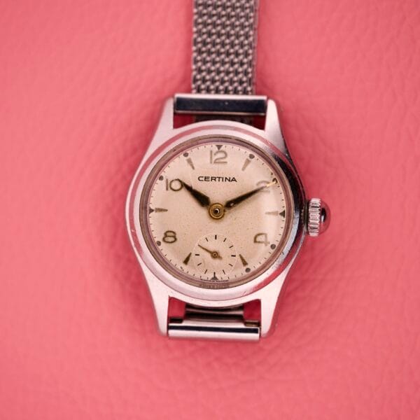 Ladies Certina Ref. 41101 wristwatch in stainless steel (Cal. 19-10) with a mesh strap, displayed on a pink textured background.