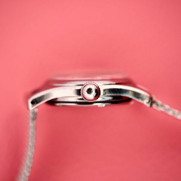 Close-up side view of the Ladies Certina Ref. 41101 in stainless steel Cal. 19-10, set against a pink background, highlighting the crown and part of the strap.