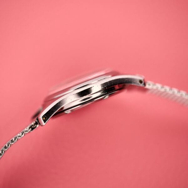 Side view of a Ladies Certina Ref. 41101 stainless steel Cal. 19-10 wristwatch with a metal band, set against a pink background.