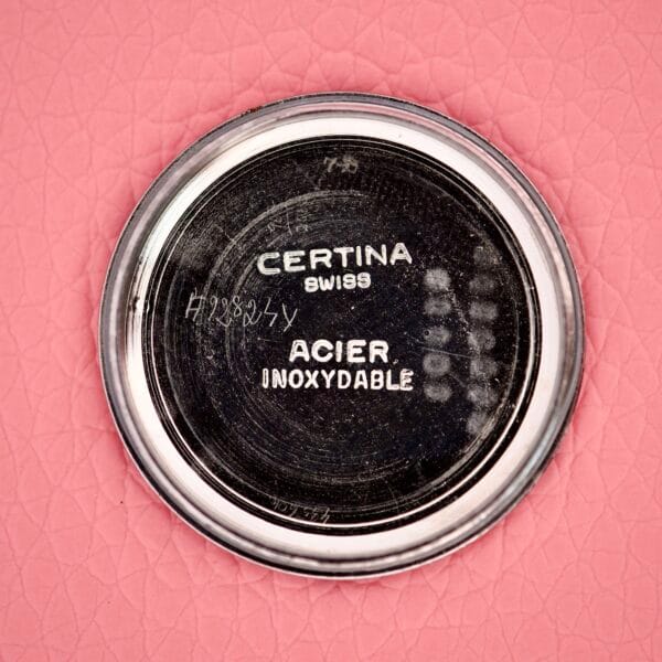 Back cover of Ladies Certina Ref. 41101 in stainless steel Cal. 19-10 on pink textured background, showing engraved Swiss and Stainless Steel markings.
