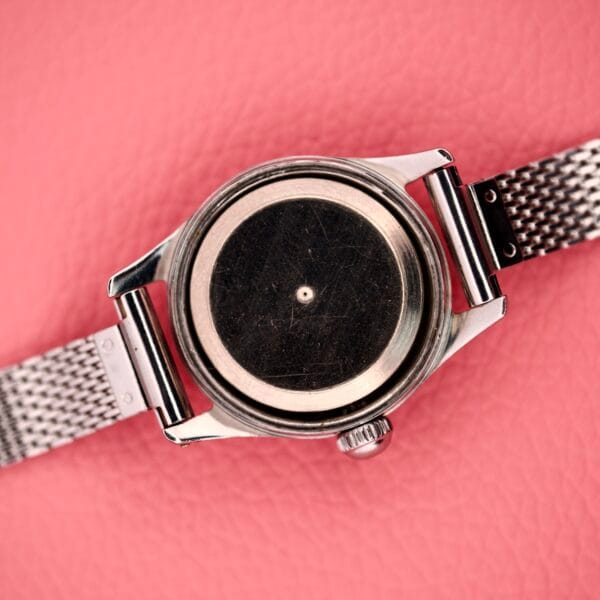 A Certina Ladies Ref. 41101 stainless steel wristwatch (Cal. 19-10) with a mesh band, displayed face down on a pink textured surface.