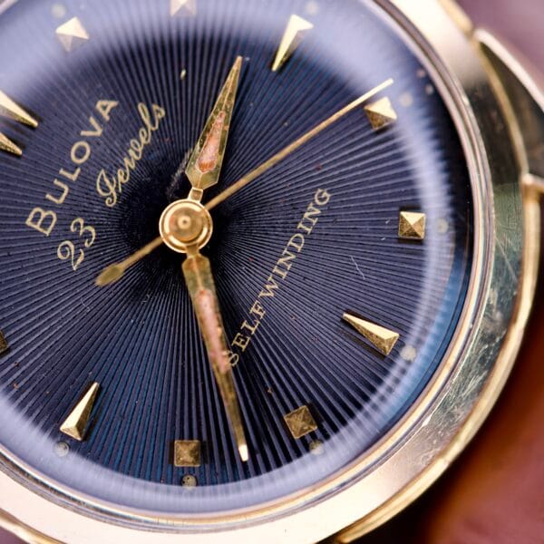 Close-up of a 1957 Bulova 23 Jewels Self Winding Cal. 10BPAC watch face featuring gold hour markers and hands.