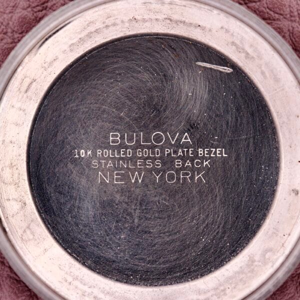 Close-up of a 1957 Bulova 23 Jewels Self Winding Cal. 10BPAC watch backplate, displaying engraved material, origin details, and the self-winding mechanism.
