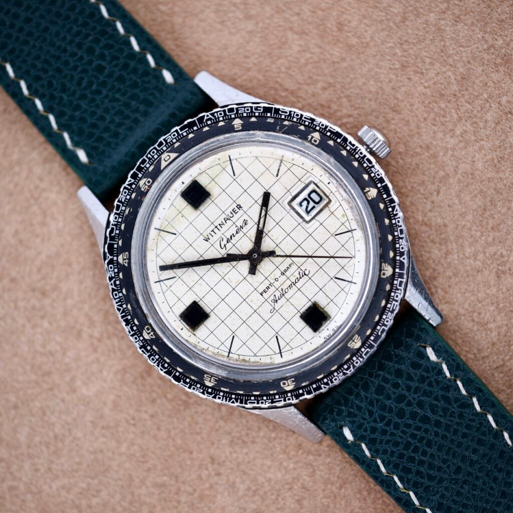 Wittnauer Pert-O-Graph Ref. 7005 with rare Pert-O-Graph Scale Bezel, grid-patterned dial, and green leather strap shown on a tan surface.