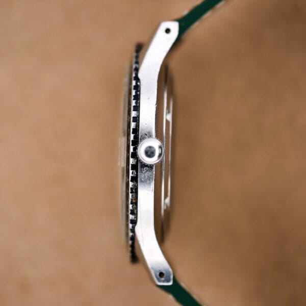 Side view of a silver Wittnauer Pert-O-Graph Ref. 7005 with crown and Rare Pert-O-Graph Scale Bezel, set against a blurred brown background.
