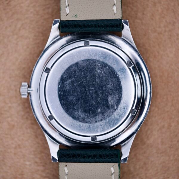 The back of a Wittnauer Pert-O-Graph Ref. 7005 Rare Pert-O-Graph Scale Bezel wristwatch with a black leather strap is shown on a tan surface.