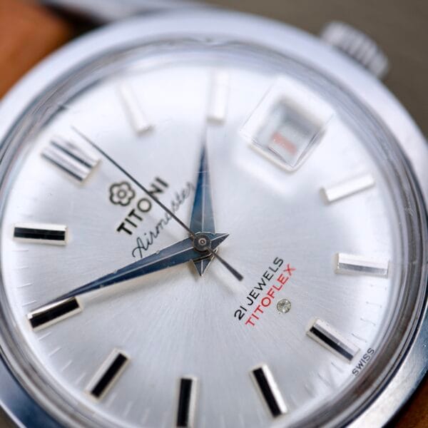 Close-up of a Titoni Air Master 305-345 Stainless Steel wristwatch with Titoflex, 21 jewels, silver dial, black hour markers, and blue hands.