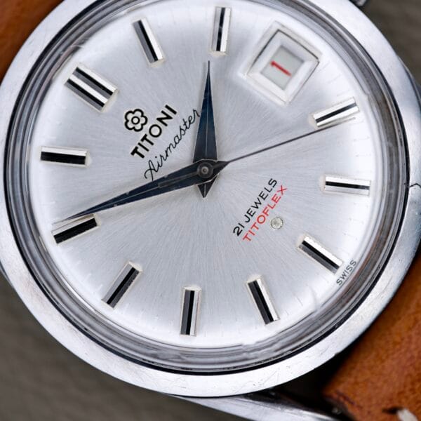 Close-up of a Titoni Air Master 305-345 with a silver dial, brown leather strap, stainless steel case, and Titoflex movement featuring 21 jewels.