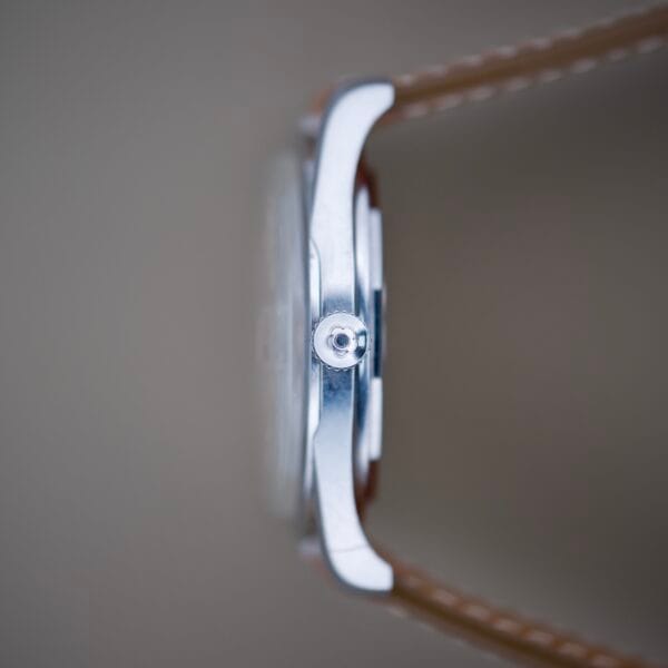 Close-up side view of a Titoni Air Master 305-345 Stainless Steel 21 Jewels Titoflex wristwatch with a brown leather strap, set against a blurred background.