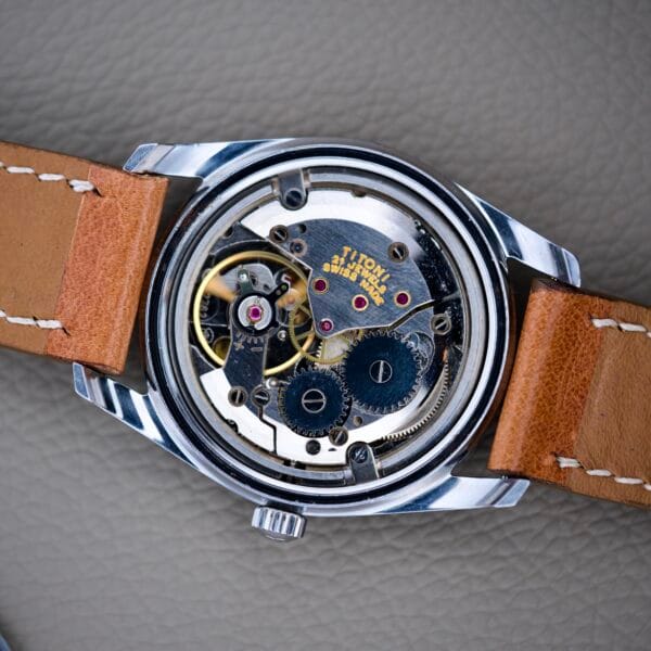 Close-up of a Titoni Air Master 305-345 Stainless Steel watch with its back cover removed, revealing the intricate gears and 21 jewels of the Titoflex movement inside.