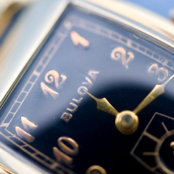 Close-up of a Bulova Art Deco Black Dial With Arabic Numerals Cal. 10 AK, showcasing gold numerals and hands on a sleek black face.