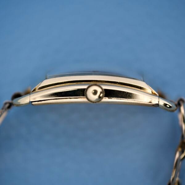 Side view of a Bulova Art Deco wristwatch, black dial with Arabic numerals (Cal. 10 AK), and round crown, photographed against a light blue background.