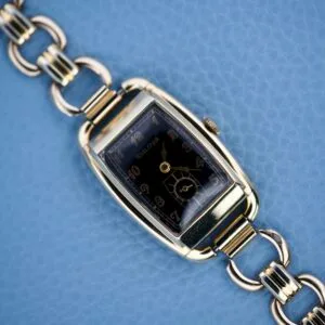 Bulova Art Deco Black Dial With Arabic Numerals Cal. 10 AK wristwatch with a rectangular face, shown on a blue textured background.