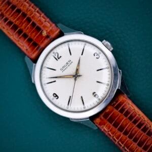 Gruen Precision White Dial from France Cal. 515SS wristwatch with a brown leather strap displayed on a teal background.