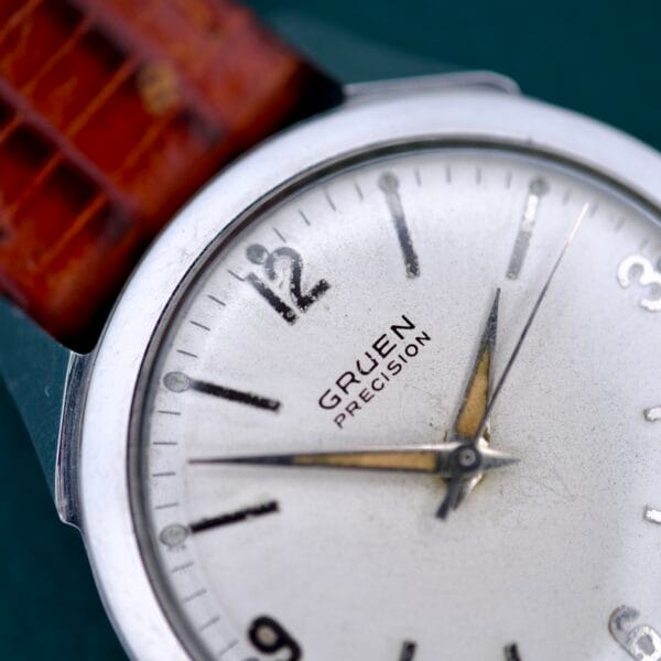 Close-up of a Gruen Precision White Dial From France Cal. 515SS wristwatch featuring a white dial, brown leather strap, and metallic hands.
