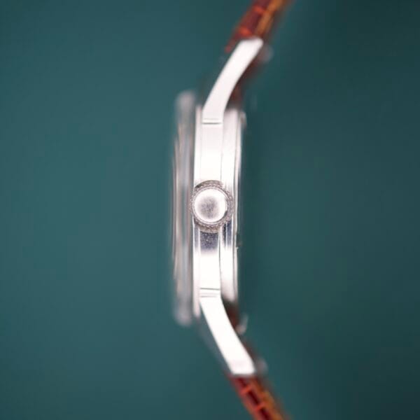 Side view of the Gruen Precision White Dial From France Cal. 515SS, featuring a silver case, brown leather strap, and white dial against a green background.