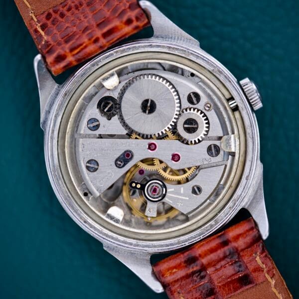Close-up of the Gruen Precision White Dial From France Cal. 515SS watch, featuring an exposed mechanical movement with visible gears and a brown leather strap.
