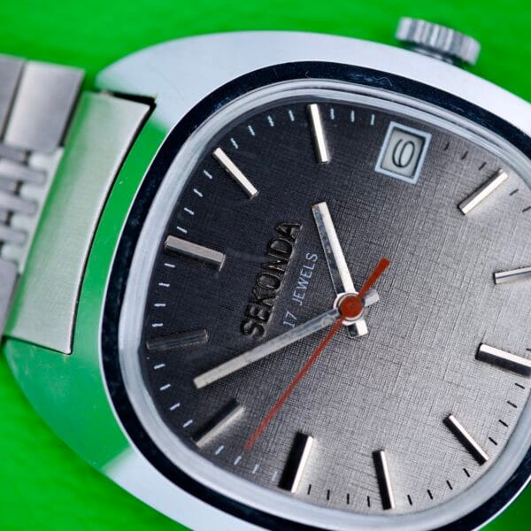 Close-up of the Seconda Ombre Grey Dial In Stainless Steel Cal. 2614 2H wristwatch, featuring a stainless steel band and ombre grey dial, set against a bright green background.