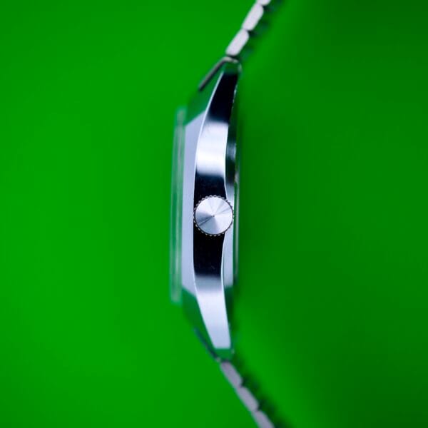 Side view of the Seconda Ombre Grey Dial In Stainless Steel Cal. 2614 2H wristwatch, featuring a stainless steel case and metal strap, displayed against a bright green background.