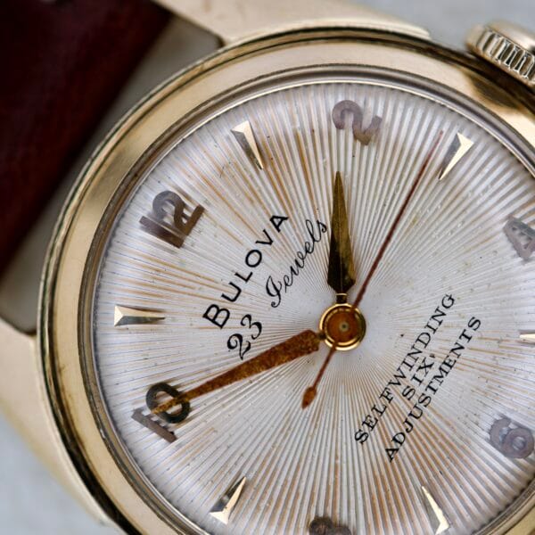 Close-up of a 1965 Bulova 23 Jewels Six Adjustments Automatic watch face, featuring gold hands and numerals that highlight its classic vintage design.