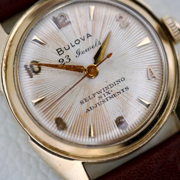 Close-up of a 1965 Bulova 23 Jewels Six Adjustments Automatic wristwatch featuring gold markers and a brown leather strap.