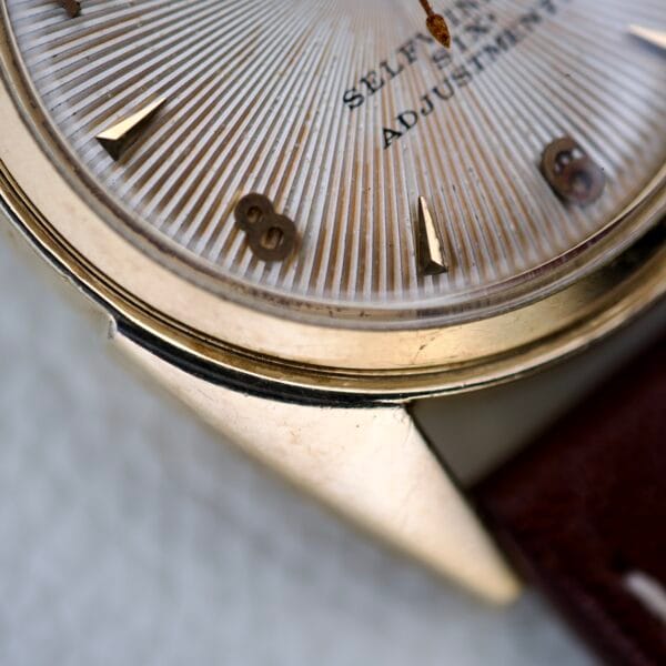 Close-up of the 1965 Bulova 23 Jewels Six Adjustments Automatic gold wristwatch featuring a textured dial and brown leather strap.