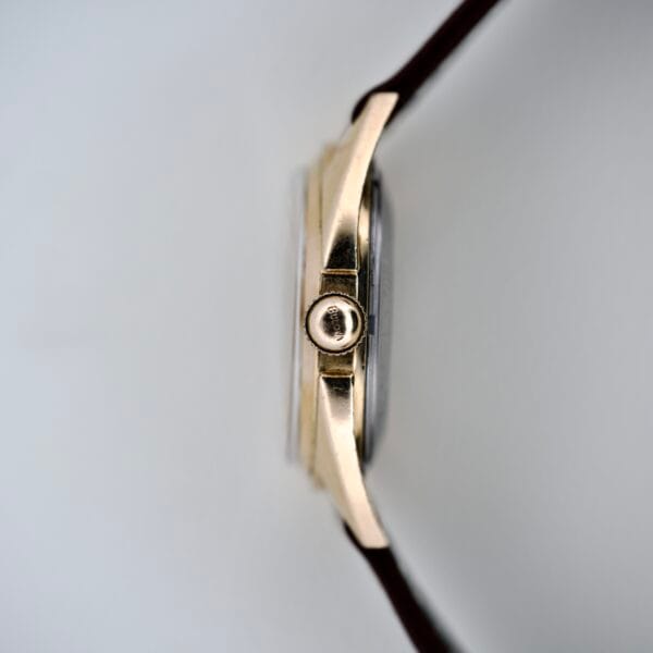 Side view of a 1965 Bulova 23 Jewels Six Adjustments Automatic gold wristwatch with a brown leather strap, set against a plain white background.
