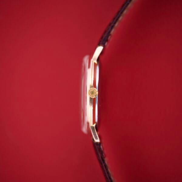 Close-up side view of Certina Ref. 7400-207 with a brown strap and Rose Gold Tone case, featuring Cal. 28-10 movement, set against a bold red background.