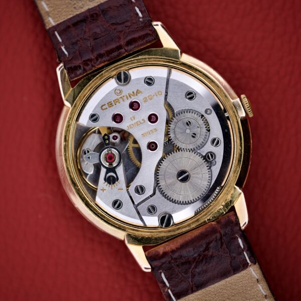 Certina Ref. 7400-207 wristwatch in Rose Gold Tone with visible Cal. 28-10 mechanical gears and a brown leather strap, elegantly displayed on a red leather surface.